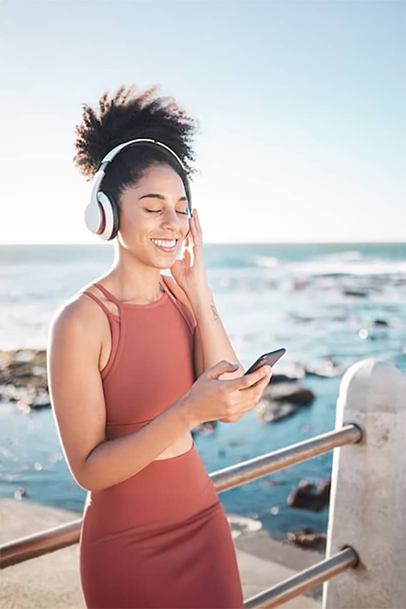 Black woman beach headphone smartphone with fitness runner listening music sports motivation happy streaming online with podcast radio phone running by sea with calm outdoor